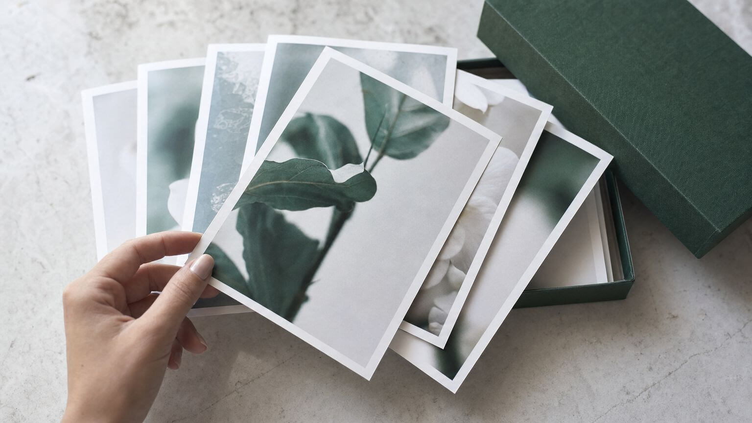 Waaier fotoprints op een licht werkblad waarvan er een wordt opgetild, naast een donkergroene archiefdoos